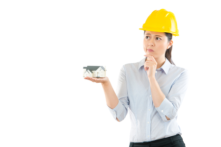 portrait of a woman builder holding house model on the copyspace thinking problem solution method with white wall empty area background about new architecture case.の写真素材