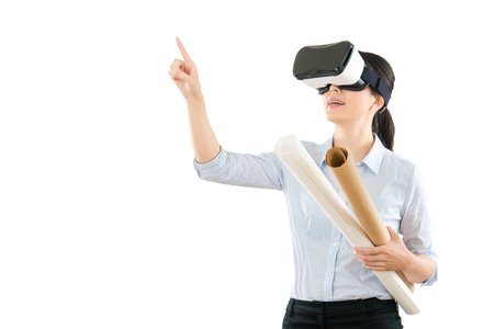 young asian architect woman holding design paper scroll experience VR virtual reality glasses and using hand finger touch screen on air copyspace on the white wall studio background.の写真素材