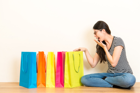 elegant girl happy receive birthday and christmas festive gifts cheerful open shopping bag sitting on wooden floor on white wall background.の写真素材