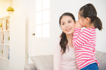 Happy asian loving mother and her daughter child girl playing and hugging. Daughter whispering to mom a secret in the living room at home. family activity concept.の写真素材