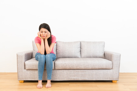 sad woman sitting on couch and weeping crying thinking of bad news after family quarreled in living room wood floor with white background.の写真素材