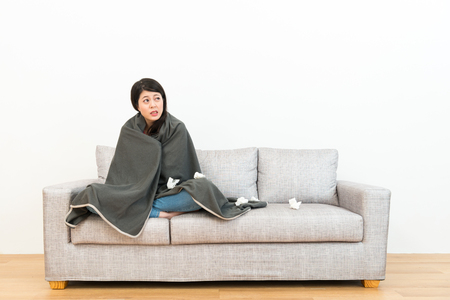 attractive beauty girl feeling cold sitting on sofa couch and looking at white background thinking solution when she catches a cold.の写真素材