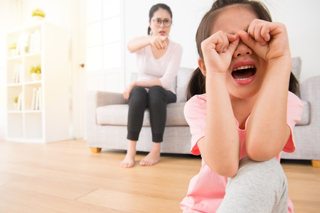 lovely asian female children so sad to crying when she was bullying in the school and the teacher on the sofa couch curse pointing to her unhappy sitting on the wooden floor.の写真素材
