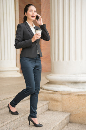 professional business lawyer using her mobile smartphone to discuss with her customers legal action and holding coffee walking in court outdoor ladder.の写真素材