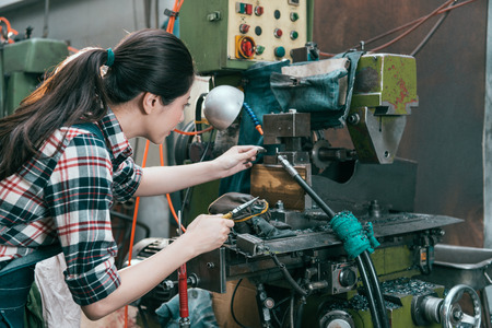 back view photo of elegant woman lathe worker working at milling machine department and using pliers tool adjusting components.の写真素材