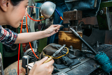 concentrated lathe female worker holding pliers ready to adjust small components in machine when working at milling machine factory.の写真素材