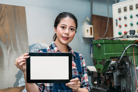 smiling lathe female worker holding mobile digital tablet computer pad and showing blank screen in milling machine drilling industry factory.の写真素材