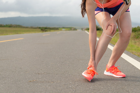 closeup of female athlete ankle injury when running on road fitness and stop to using hand hold painful position with beautiful background.の写真素材