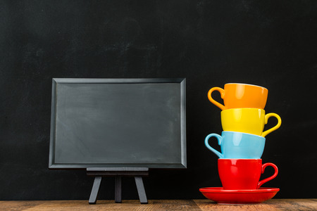 colorful ceramic coffee cups stacked together with small blackboard on wooden floor ground in black wall background show restaurant advertising area.の写真素材
