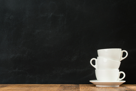 ceramic clean latte coffee cups stacked in blackboard wall background and showing copyspace for advertising text content with wood texture surface floor.の写真素材