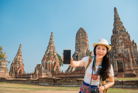 traveler woman showing modern mobile smartphone blank screen in Wat Chaiwatthanaram, Thailand, Asia. Girl holding empty smartphone screen on travel with copyspace.の写真素材