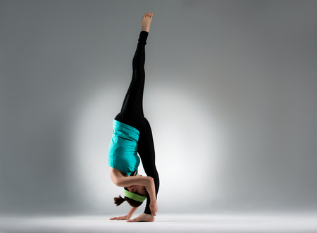 elegant bodybuilding woman single feet standing on gray background floor inverted and one feet extend show perfect yoga gesture in fitness studio classroom.の写真素材