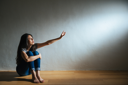 battered abused woman concept of lonely victim sitting on white background wood floor in dark and sadness looking at light need help.