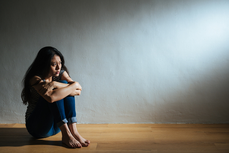 sadness young woman sitting on wood floor looking at empty dark area feeling unhappy and afraid on white wall background with battered abused woman concept.の写真素材