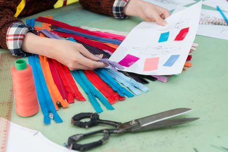 closeup photo of fashion studio female designer choosing zipper confirm design sketch.