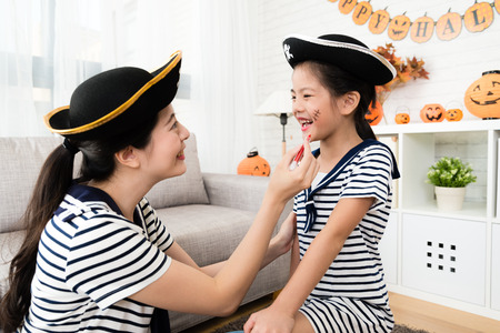 pirate girl and mother have fun with Halloween makeup drawing scars on the face at homeの写真素材