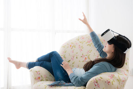 beautiful smiling woman lying down on sofa relaxing and using VR technology goggles experiencing 3D video game.の写真素材