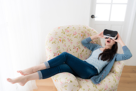happy cheerful woman using virtual reality device playing video game and lying down on sofa chair enjoying 3D simulation viewing.の写真素材
