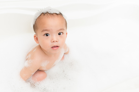 smiling happy little boy children face to camera and sitting in foam bubble water bathtub with high angle view photo on bathroom at home.の写真素材