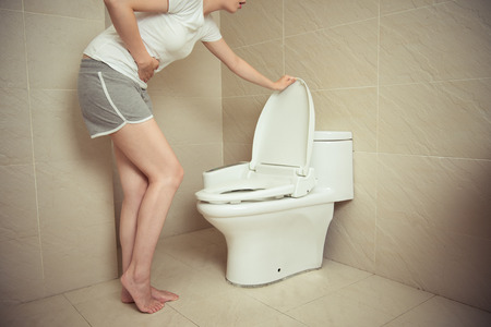 lovely young woman standing in front of toilet and using hand pressing painful position when she...