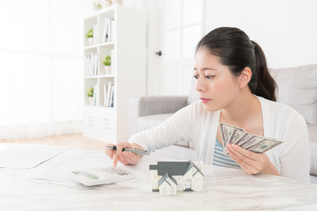 beauty sweet woman using calculator counting her savings banknote in living room when she want to buying new house for family.の写真素材
