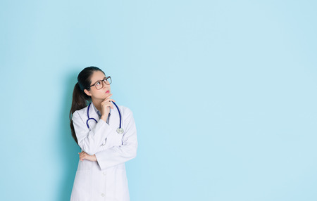 beautiful professional female doctor daydreaming healthy care medical problem solution isolated in blue wall background hospital and confused looking at empty area.の写真素材