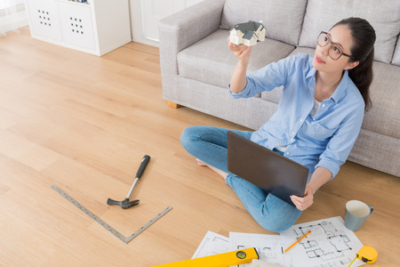 high angle view photo of smiling pretty designer holding house model researching building construction thinking refitting plan and using mobile computer design sketch drawing.の写真素材