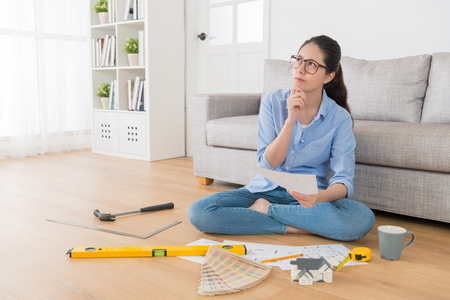 attractive happiness female design department student sitting on wooden floor doing homework and holding drawing sketch paper thinking house interior decoration in living room at home.の写真素材