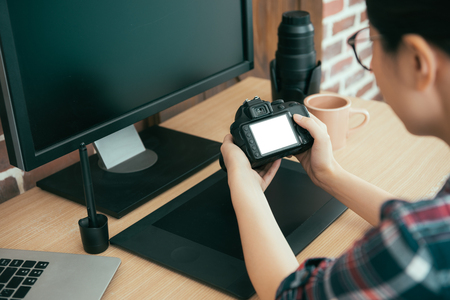 closeup back view of female business photographer holding professional camera review working picture and checking photo design style in editing office desk.の写真素材