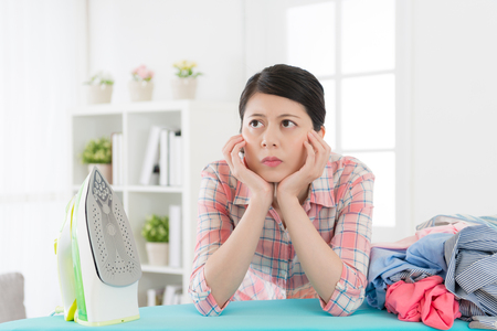 pretty elegant housewife ironing clothing feeling boring and leaning on board thinking how to fast doing housework method.の写真素材