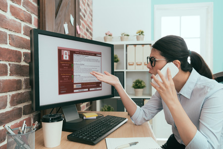 professional business woman using mobile smart phone calling for help when her company working computer getting virus invasion.の写真素材