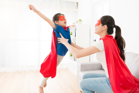 pretty young mother holding cute little girl making fly posing and playing as superhero at home.の写真素材