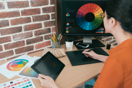back view photo of pretty young female designer holding mobile computer working and using digital pad pen drawing design.の写真素材