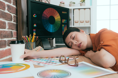 beautiful young graphic design company female employee working long time and lying down on office desk sleeping resting.の写真素材