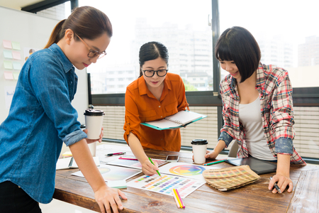 young beautiful female design team worker discussing new product plan and looking at palette paper document choosing main color during meeting.の写真素材