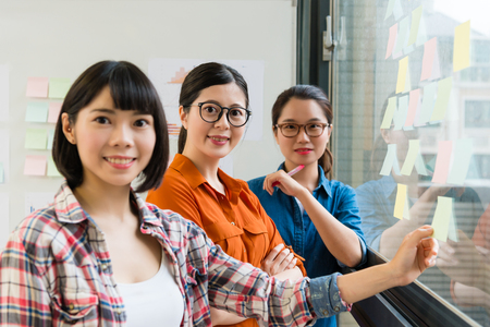 confident pretty female business team meeting on glass wall and looking at camera smiling.の写真素材