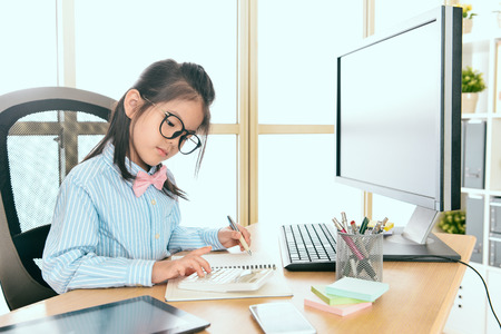 beautiful young little business worker using calculator counting company marketing money and record on notebook when she sitting in workplace.