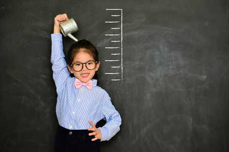 confidence happy girl kid face to camera smiling and irrigating body measured growth height isolated on black chalkboard background.