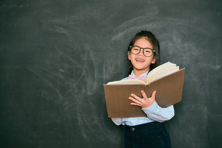 happy sweet little english teacher using study book teaching student during school class and standing in blackboard background.の写真素材