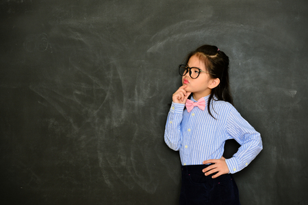 pretty young female little teacher looking at empty area feeling confused when she standing in blackboard background teaching having difficulty problem.の写真素材