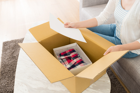 woman sitting on sofa at home opening personal online shopping parcel package and holding order list paper to confirm goods.の写真素材