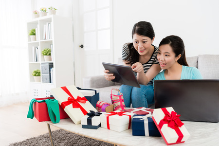 smiling attractive girls using mobile pad computer online shopping together and pointing screen to choosing summer sale goods at home.の写真素材