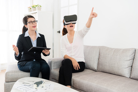 smiling friendly house agent explaining building design when her client using VR technology...