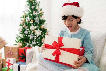 little cute Asian girl feel surprised face expression after she open the Christmas gift box sitting one sofa at home.の写真素材