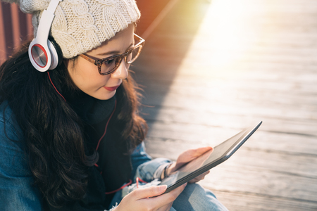 above view of beautiful young Asia student searching information online with a digital tablet sitting on the wood floor of the bridge.の写真素材