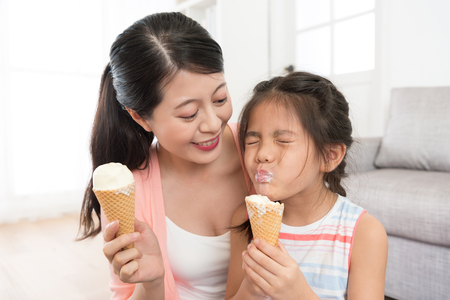 smiling beautiful mother looking at pretty little daughter eating ice cream feeling happiness and enjoying summer season at home together.の写真素材