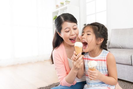 cheerful family of beautiful mother with cute daughter eating ice cream at home and playing fun together in living room.の写真素材