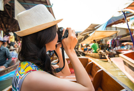 Beautiful attractive female traveler travel in Thailand and using camera to taking picture when she visiting famous floating marketの写真素材