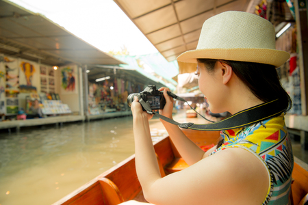 young pretty woman tourist sitting on river boat using camera recording local vendor view landscape during Thailand travel in Damnoen Saduak floating market.の写真素材