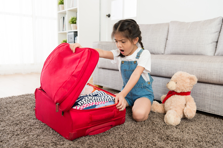 pretty beauty female children opening personal travel luggage suitcase and looking at clothing finding wrong feeling surprised.の写真素材